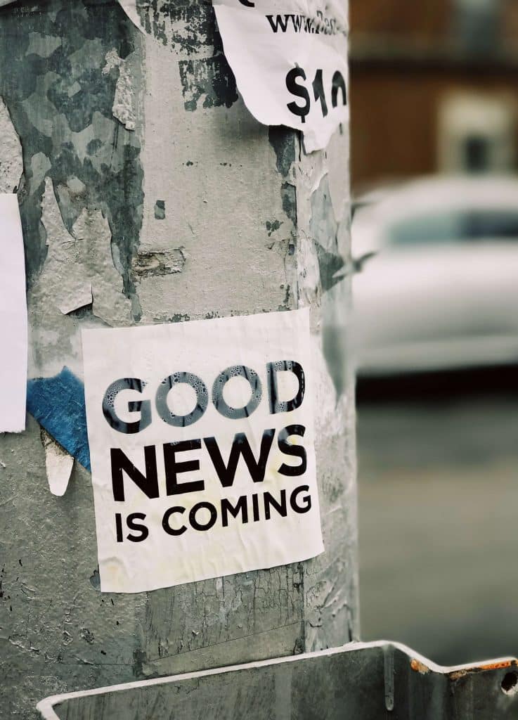 Street pole with a piece of paper taped on it saying "GOOD NEWS IS COMING"
